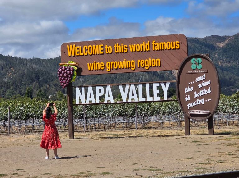 Visitor standing near the Napa Valley welcome sign at the entrance of the wine region